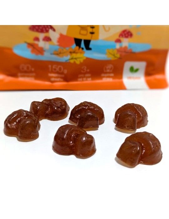 Gominolas marrones con forma de seta frente a su envase naranja de MycoGummies de 150g con ilustraciones de bosque.
